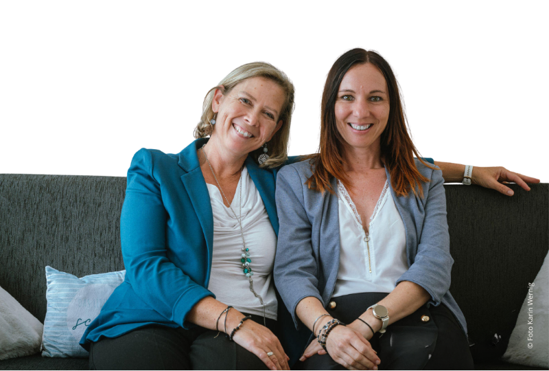 Martina Klein und Marion Zdesar sitzen auf einer Bank und lächeln